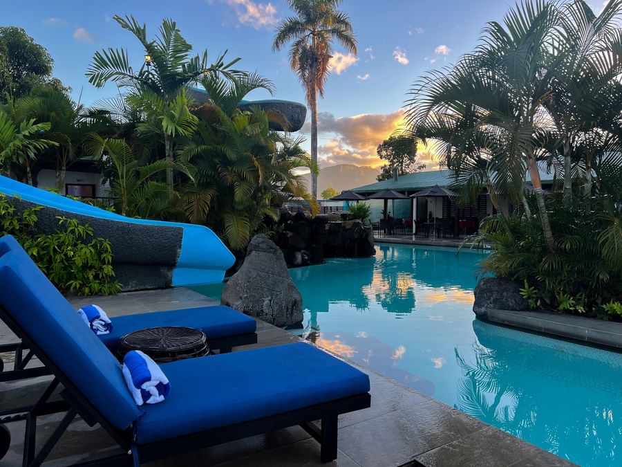 Blue poolside loungers by a rock waterfall and a water slide under a palm tree at TokaToka Resort Nadi Fiji