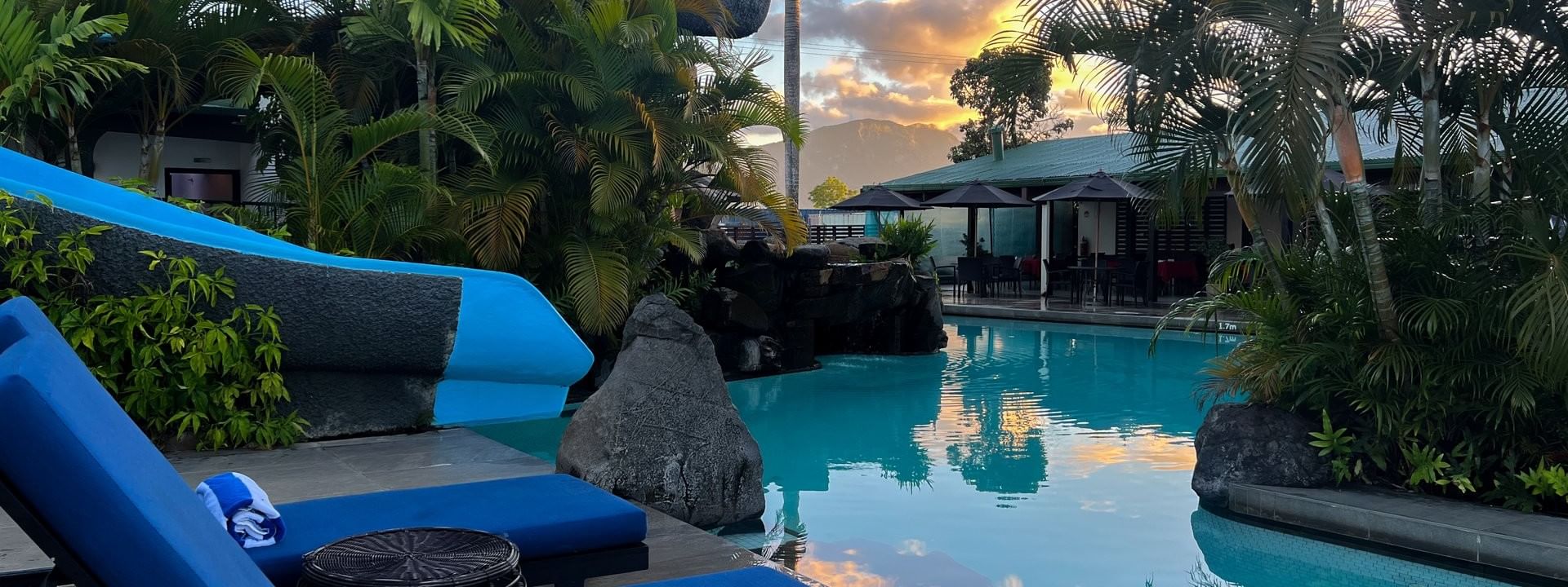 Blue lounge chairs by a swimming pool surrounded by tropical trees at Tokatoka Resort in Nadi, Fiji