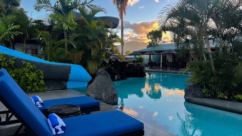 Blue lounge chairs by a swimming pool surrounded by tropical trees at Tokatoka Resort in Nadi, Fiji.