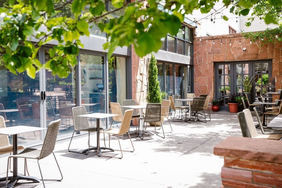 Woven chairs by white tables under green tree leaves near a stone wall at Warwick Denver
