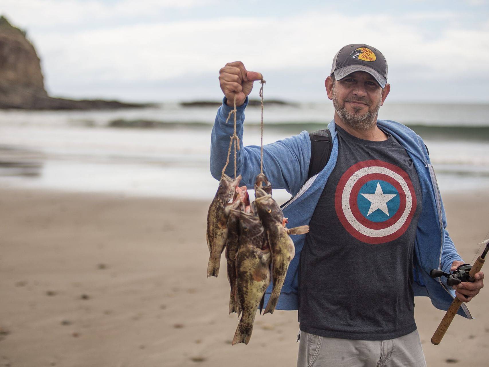 Man by a sandy beach holding fish under a cloudy sky near Morgan's Rock Reserve & Ecolodge