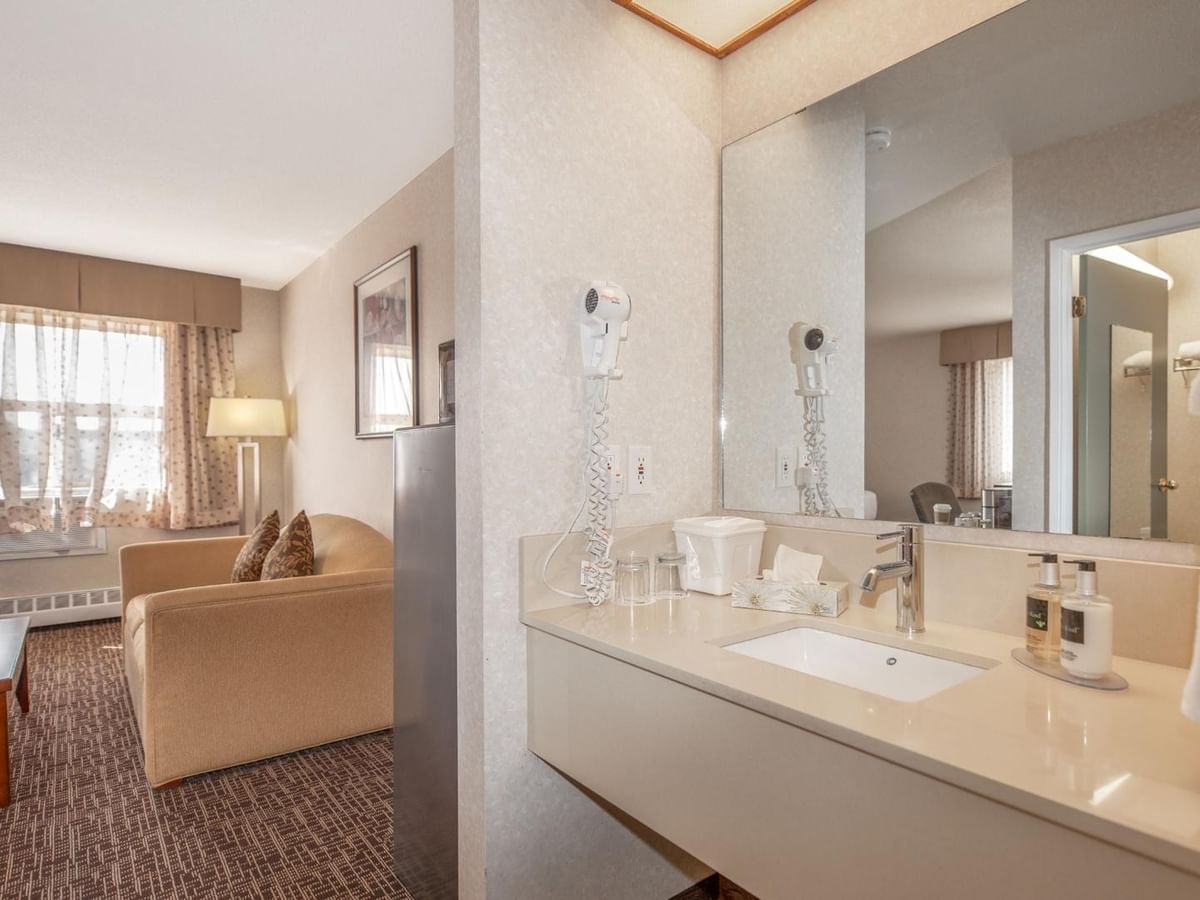 Hotel room with couch, coffee table, and a bathroom with sink, mirror, and hair dryer.