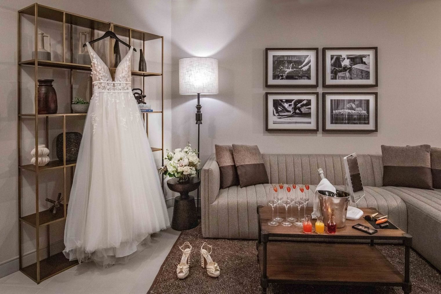 Wedding dress on a hanger, heels on the floor, couch, table with wine glasses, and three framed photos on the wall.