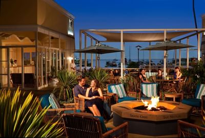 People relaxing by a fire pit at a coastal outdoor terrace in Pavilion Hotel in Avalon Catalina