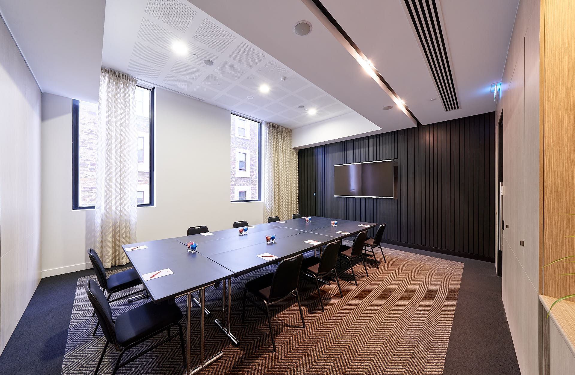 Boardroom set up facing the wall-mounted TV and carpet floors in The Hub at Ibis Adelaide