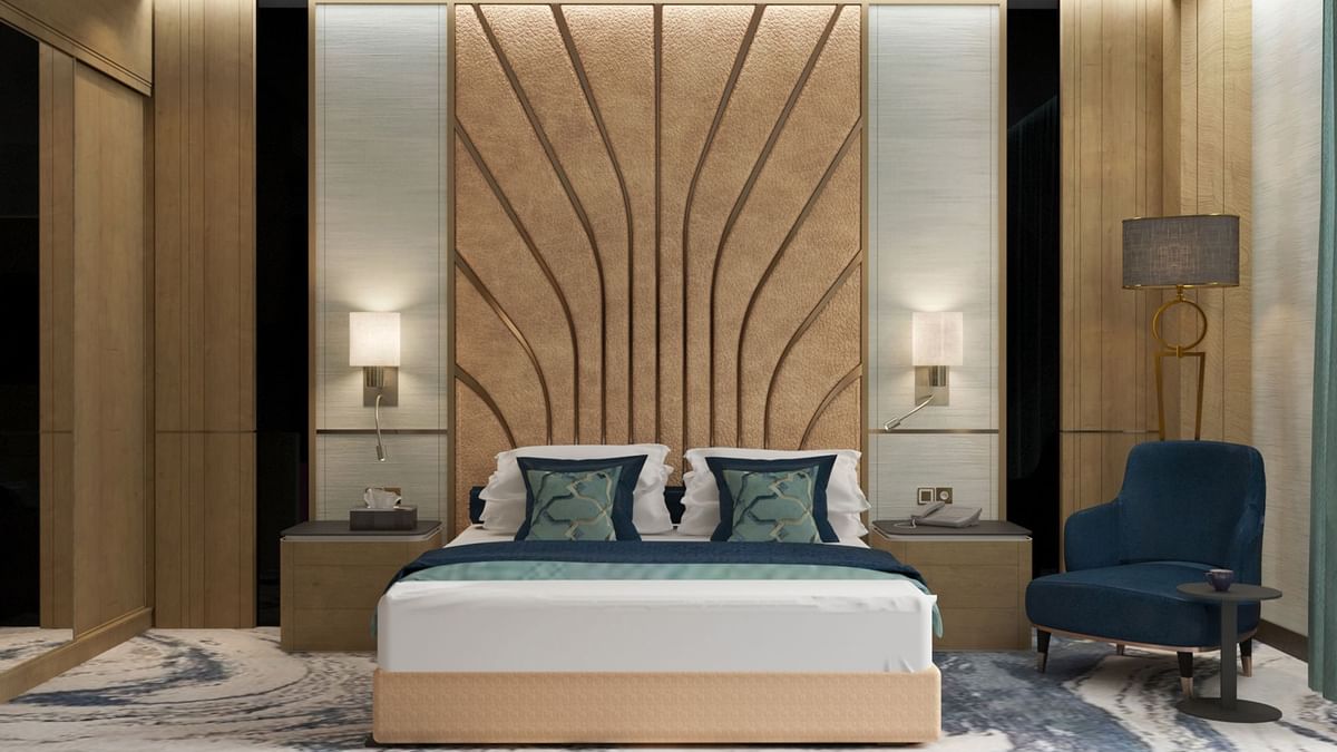 Modern bed with a patterned headboard by a blue chair in the Ambassador Suite at Cantonal Hotel by Warwick Riyadh