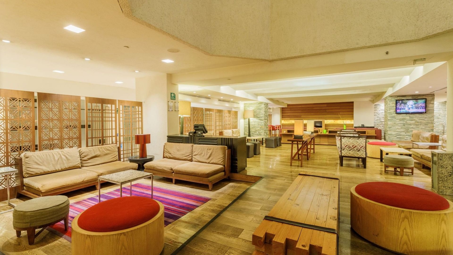 Área de lounge con biombos de madera, sofás y taburetes tipo otomán en Camino Real Aeropuerto México