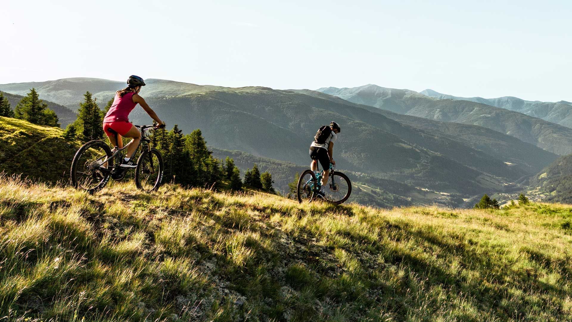 Zwei Radfahrer auf einem Bergpfad inmitten einer hügeligen Landschaft.