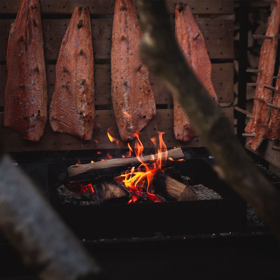 Salmon filets smoking over a wood fire at Salmon Smokehouse near Falkensteiner Hotel & Spa Carinzia