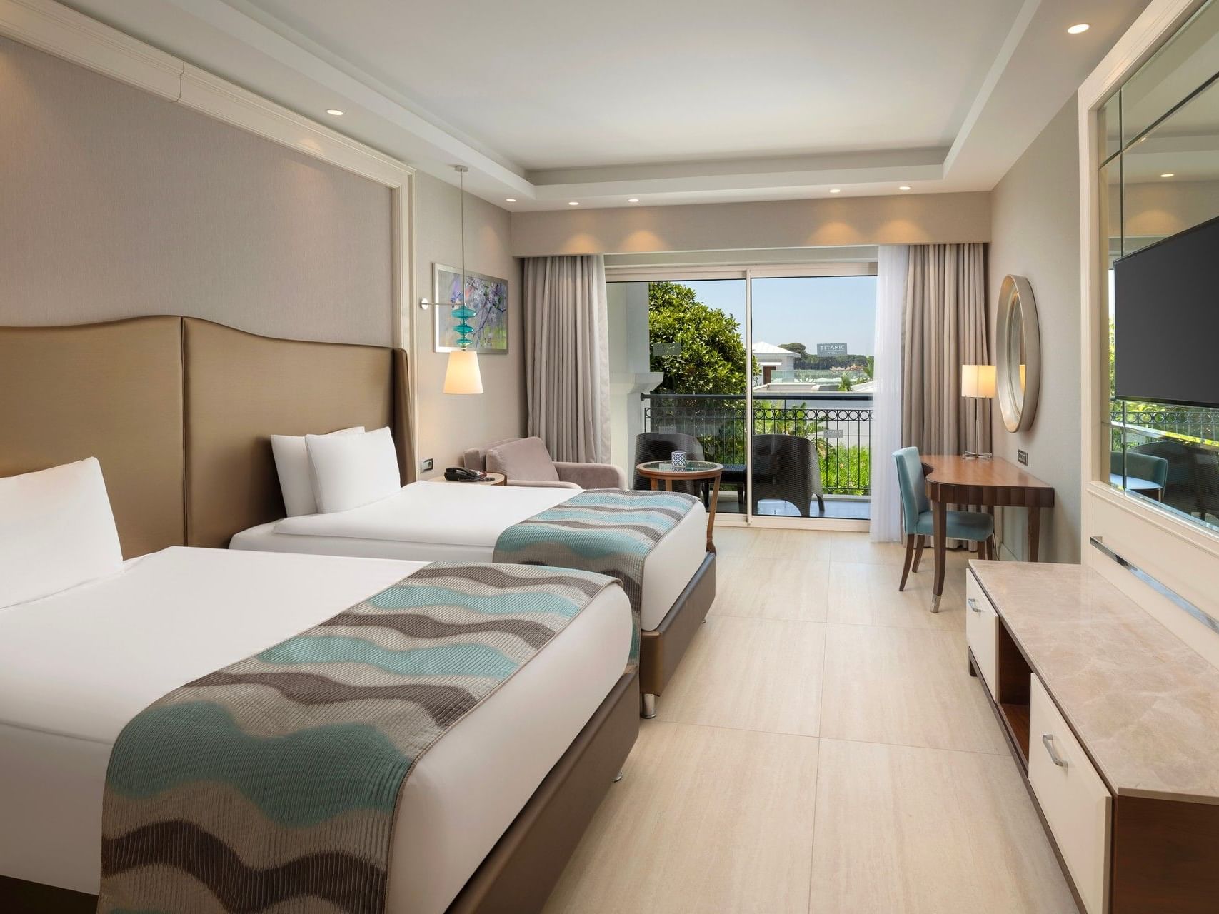 Modern hotel room with twin beds, balcony view, and contemporary furnishings at Titanic Deluxe Golf Belek