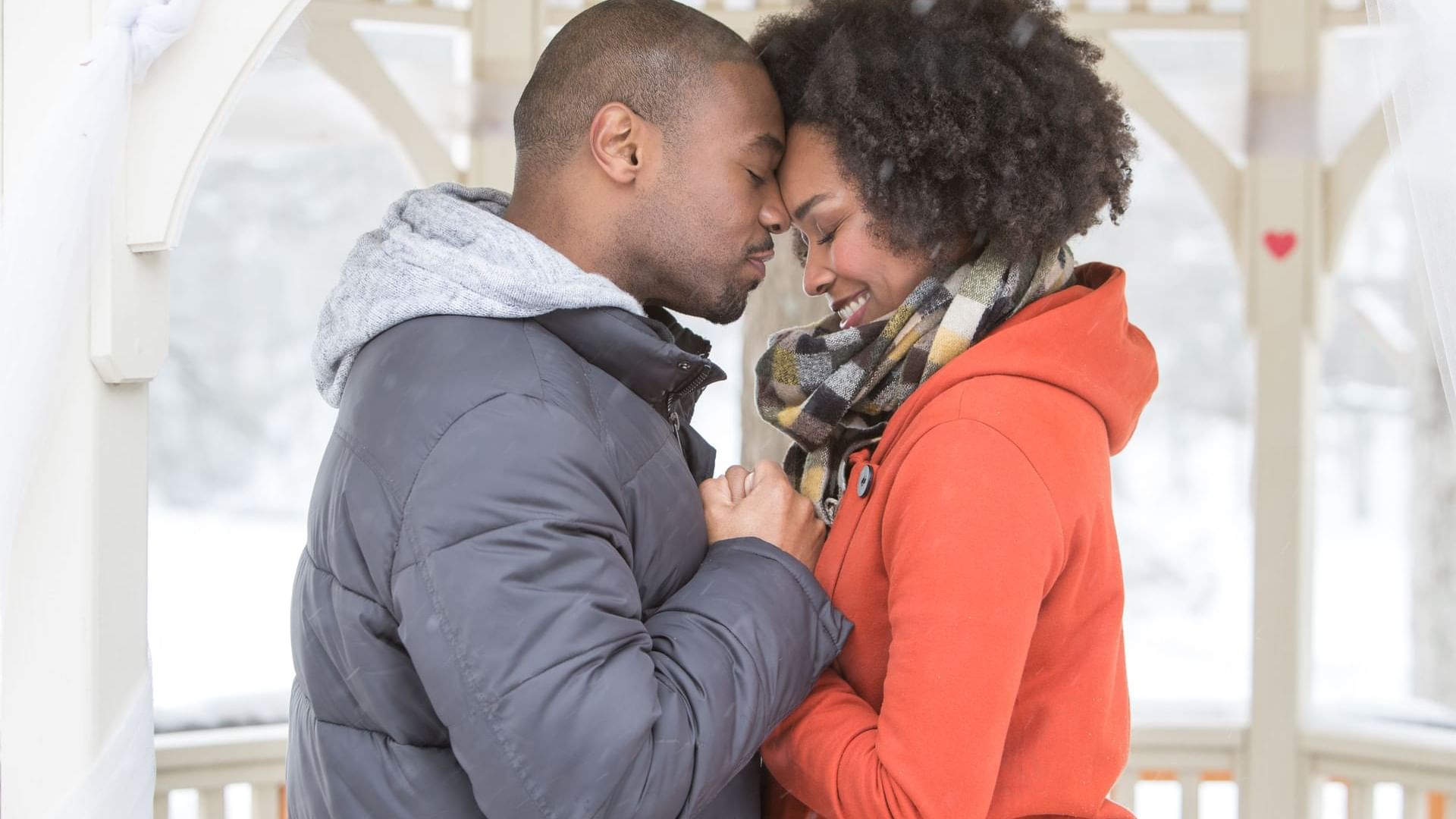 Couple with their faces against each other, while holding hands on a gazebo during winter at Cove Pocono Resorts