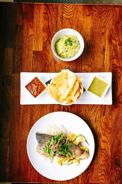 Plate of fish and salad, guacamole, chips, salsa, and sauce on a wooden table at Elevation Resort Spa