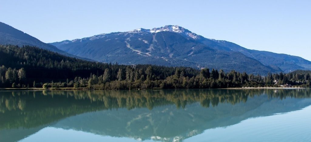 Alta Lake reflects Whistler’s mountain views on a calm day surrounded by forest and clear sky