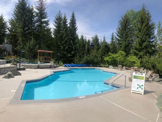 Outdoor pool with sun lounges surrounded by pine trees at Blackcomb Springs Suites