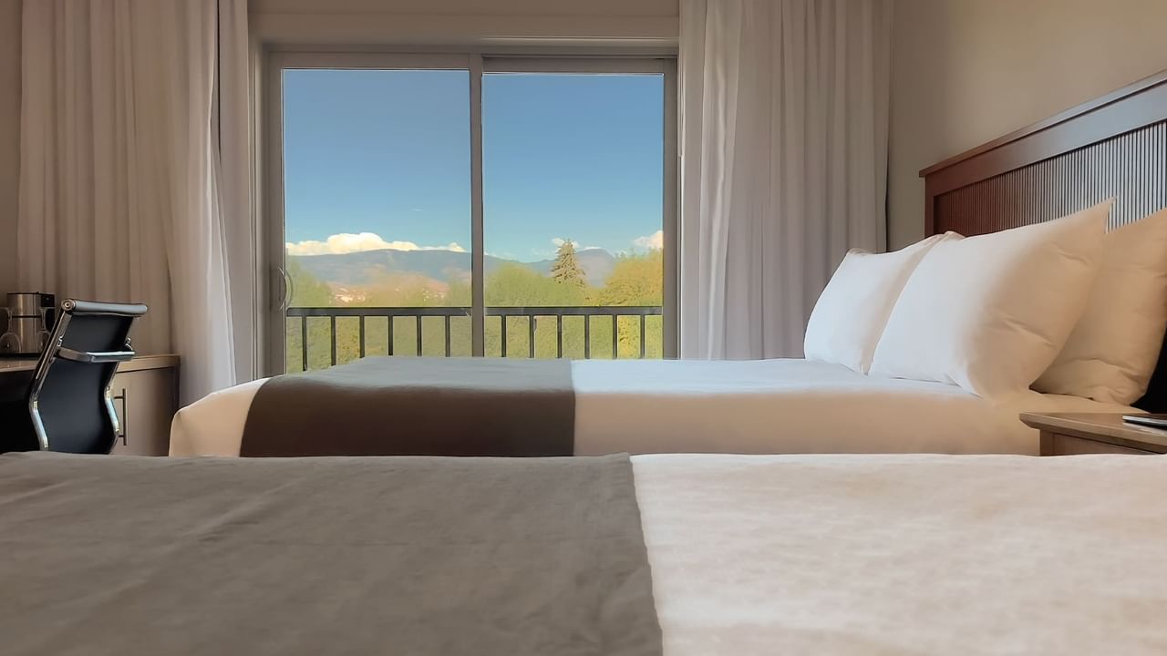 Guest room with two queen beds, balcony chair and desk