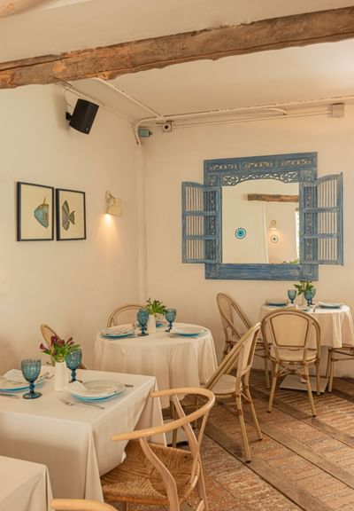 Naous Aegean Bistro Dining room with wicker chairs & white tables under a blue carved mirror at 5Q House Chapinero