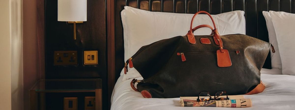 Collection Superior hotel bedroom with luggage and newspaper on bed promoting a lifestyle overnight shot.