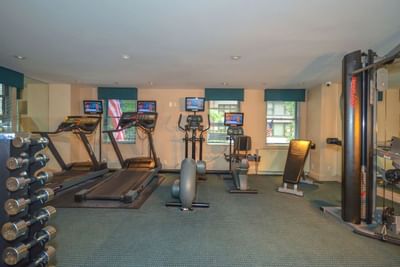 Interior of gym with treadmills, stationary bikes, weights, and other exercise equipment, with windows and American flag.