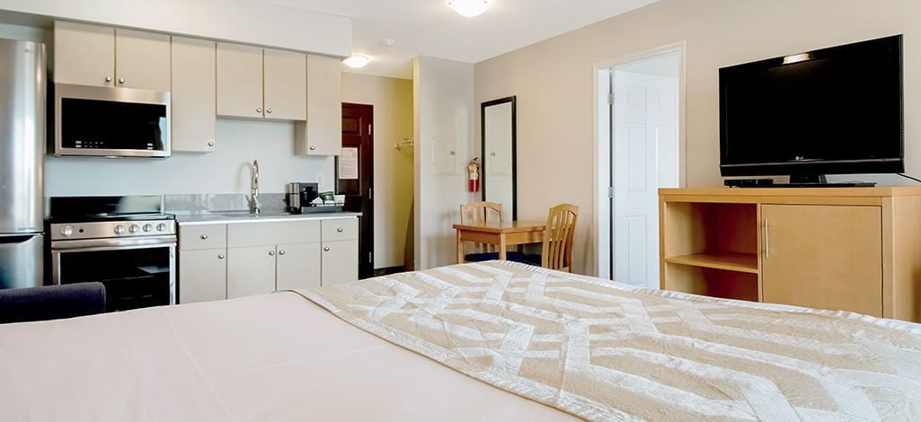 Hotel suite featuring a kitchenette, a small dining table for two, a bed, and a TV on a stand