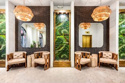 Modern lobby at The Riverwalk Plaza Hotel with wooden chairs, stylish mirrors, lush greenery display, and pendant lights