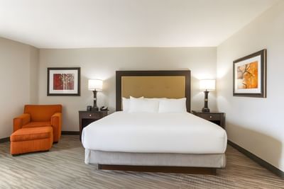 King bed with tan headboard, orange armchair, and warm bedside lamps in Premium King Room at Branson Hillside Hotel