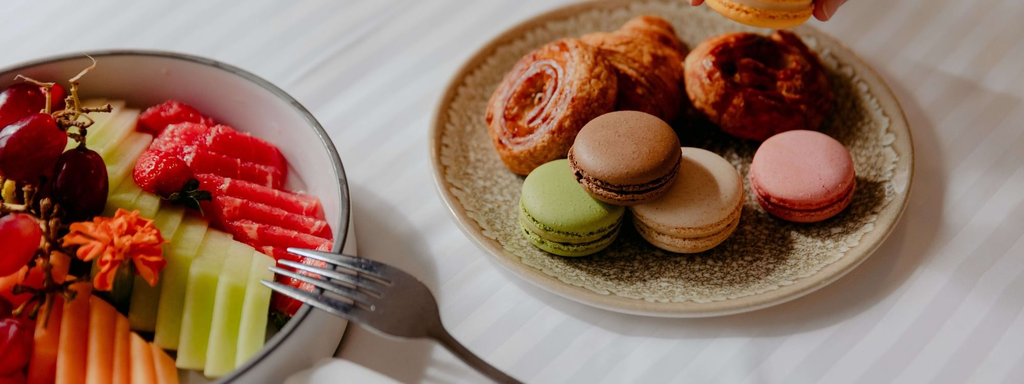 In-room dining at Novotel Sydney Parramatta, hand holding a macaron over a plate of pastries, beside a fruit bowl