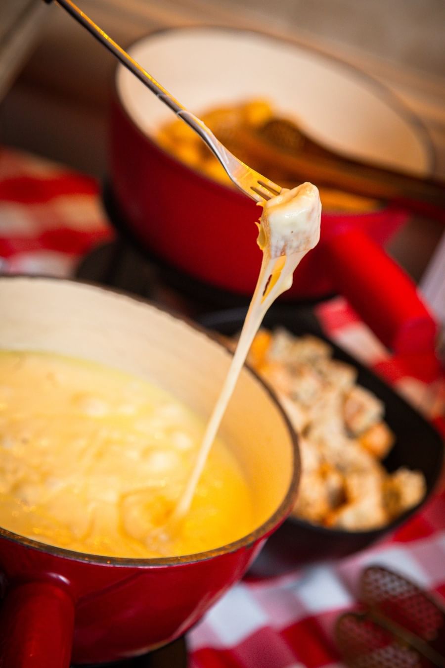 Swiss cheese fondue with a melted cheese-coated bread cube lifted on a fork above simmering pot at Téséo Restaurant & Bar