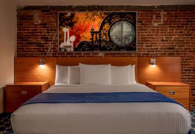 Bed between side tables against an exposed brick wall with art in King Atrium View at Harborside Inn Boston