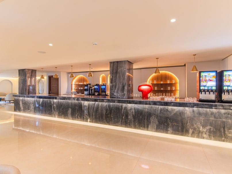 Modern bar counter with marble top, beverage machines, arched shelves, and decorative lighting in a sleek interior.