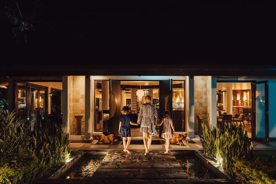Family walks toward a brightly lit resort entrance across a stone path at warwick le lagon-vanuatu