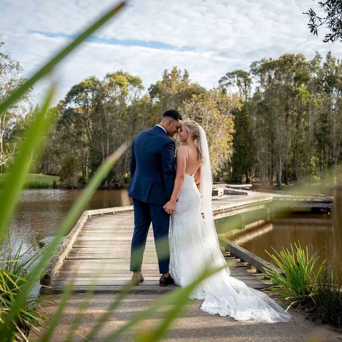 Wedded couple embrace on a bridge by Kooindah Lake at Mercure Kooindah Waters