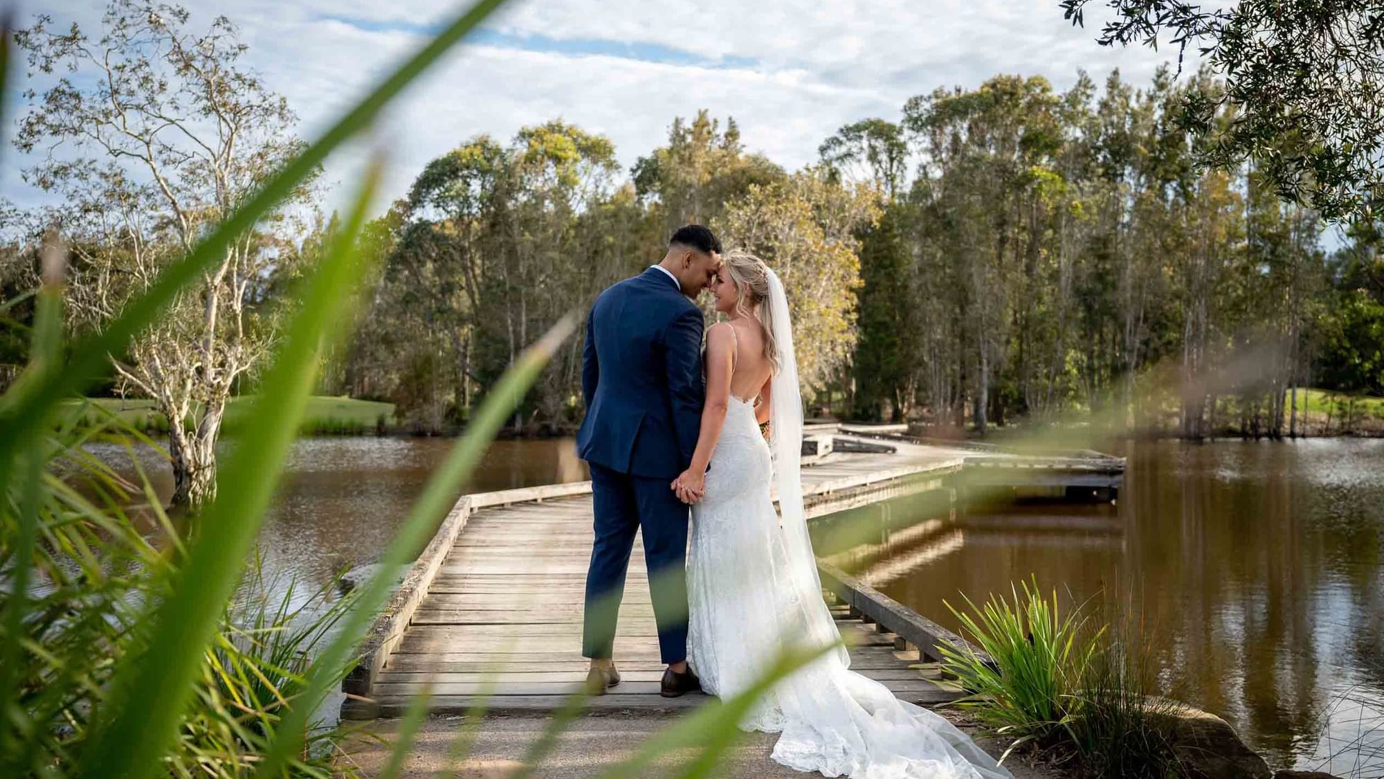 Wedded couple embrace on a bridge by Kooindah Lake at Mercure Kooindah Waters