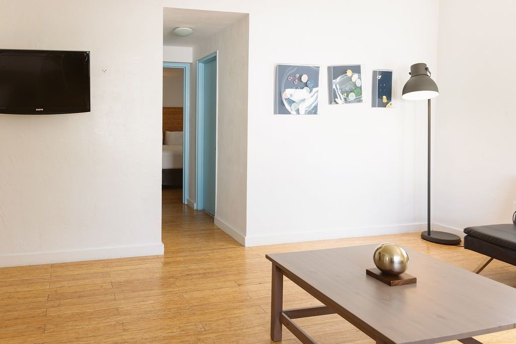A wide view of a living room with a sofa, coffee table, lamp, and TV on a white wall with artwork.