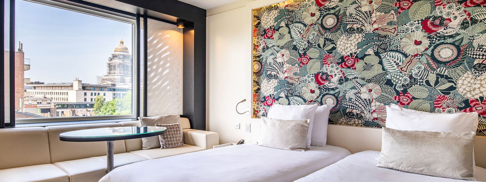 Two beds with seating by the window offering city views in the Superior Twin at The Hotel Brussels