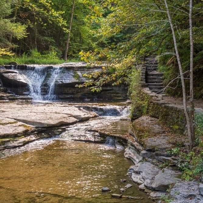 Stone steps and a path ascend a terraced rock on the Ithaca hiking trail to a waterfall near La Tourelle Hotel and Spa