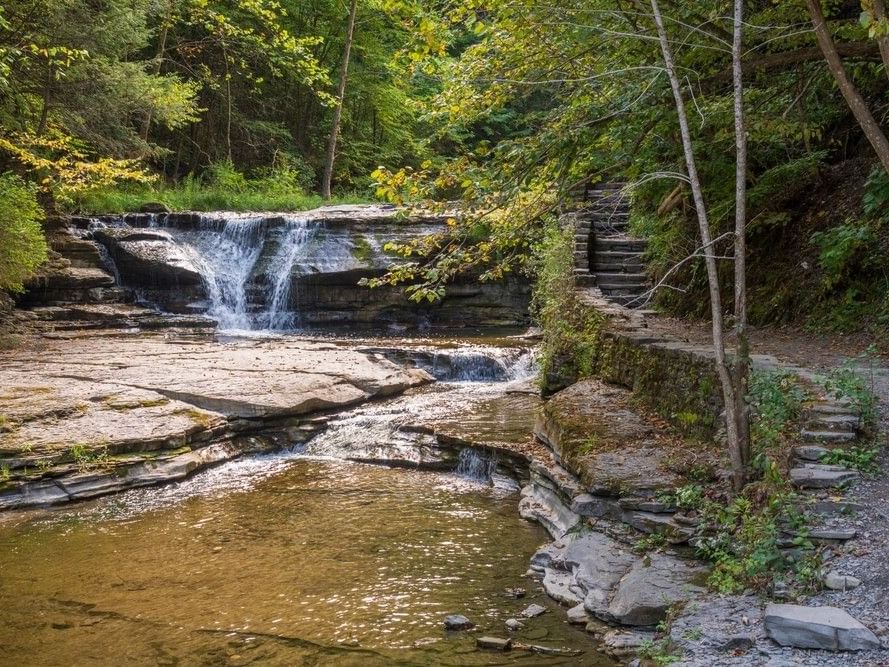 Stone steps and a path ascend a terraced rock on the Ithaca hiking trail to a waterfall near La Tourelle Hotel and Spa