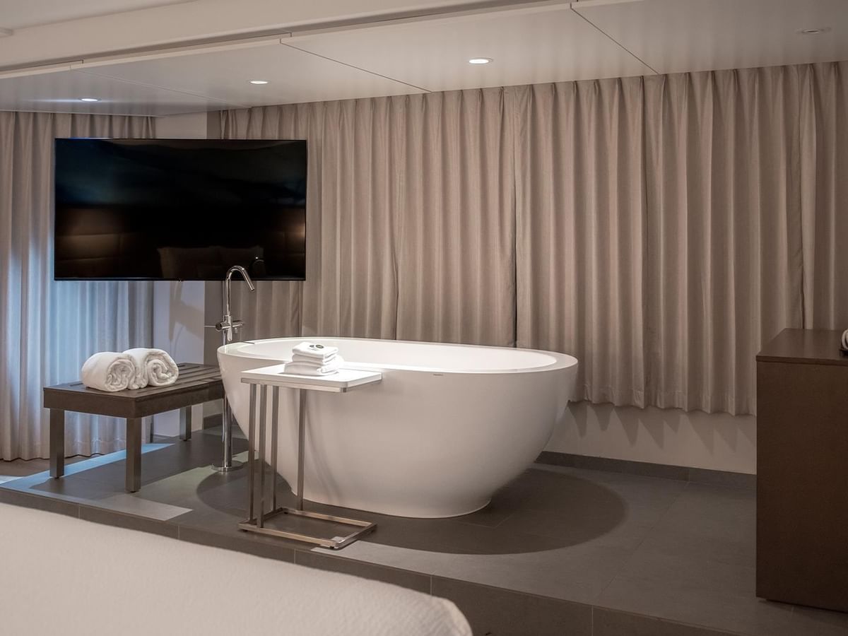 White freestanding bathtub with TV behind curtains in Coast Premium King Suite at Coast Bastion Hotel Nanaimo.