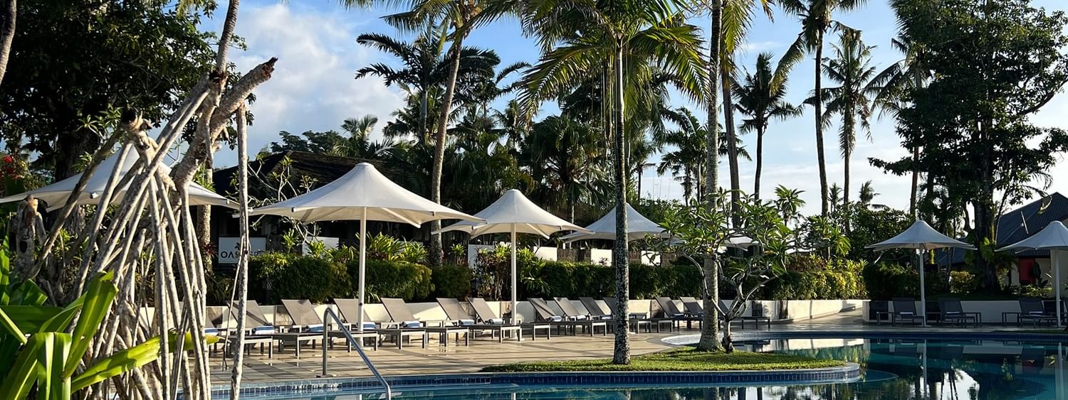 Swimming pool with sun loungers under umbrellas surrounded by tropical trees at Warwick Le Lagon Vanuatu Efate
