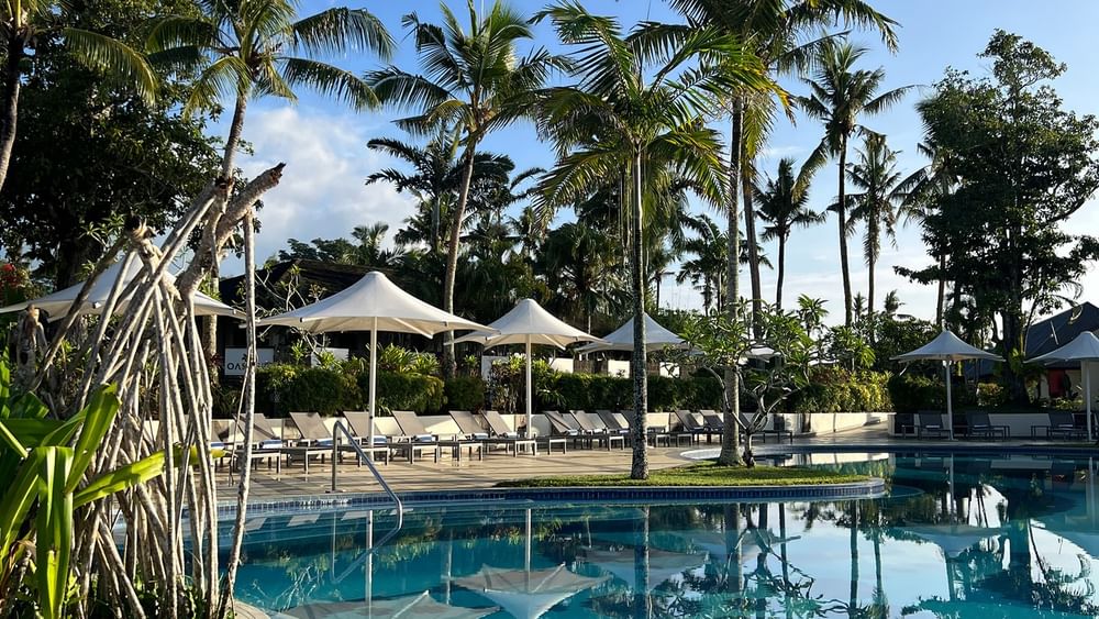 Swimming pool with sun loungers under umbrellas surrounded by tropical trees at Warwick Le Lagon Vanuatu Efate.