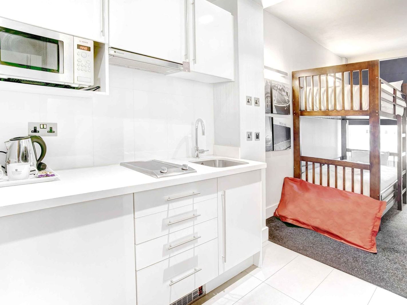 The Family King Suite at Sandman Signature Newcastle Hotel with two bunk beds and a pantry with kitchen supplies and white pantry cupboards 