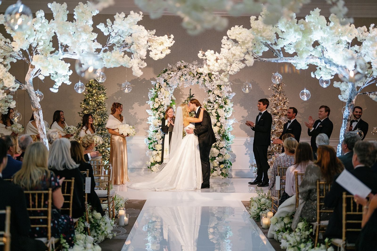 Wedding couple by a floral arch under white blossom trees and hanging glass globes at Warwick Melrose Dallas
