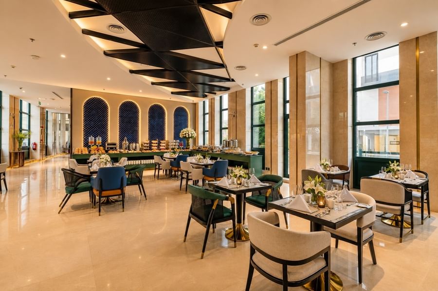 Dining tables with white napkins and chairs near the breakfast buffet in Roshen Restaurant at Naviti by Warwick Jeddah