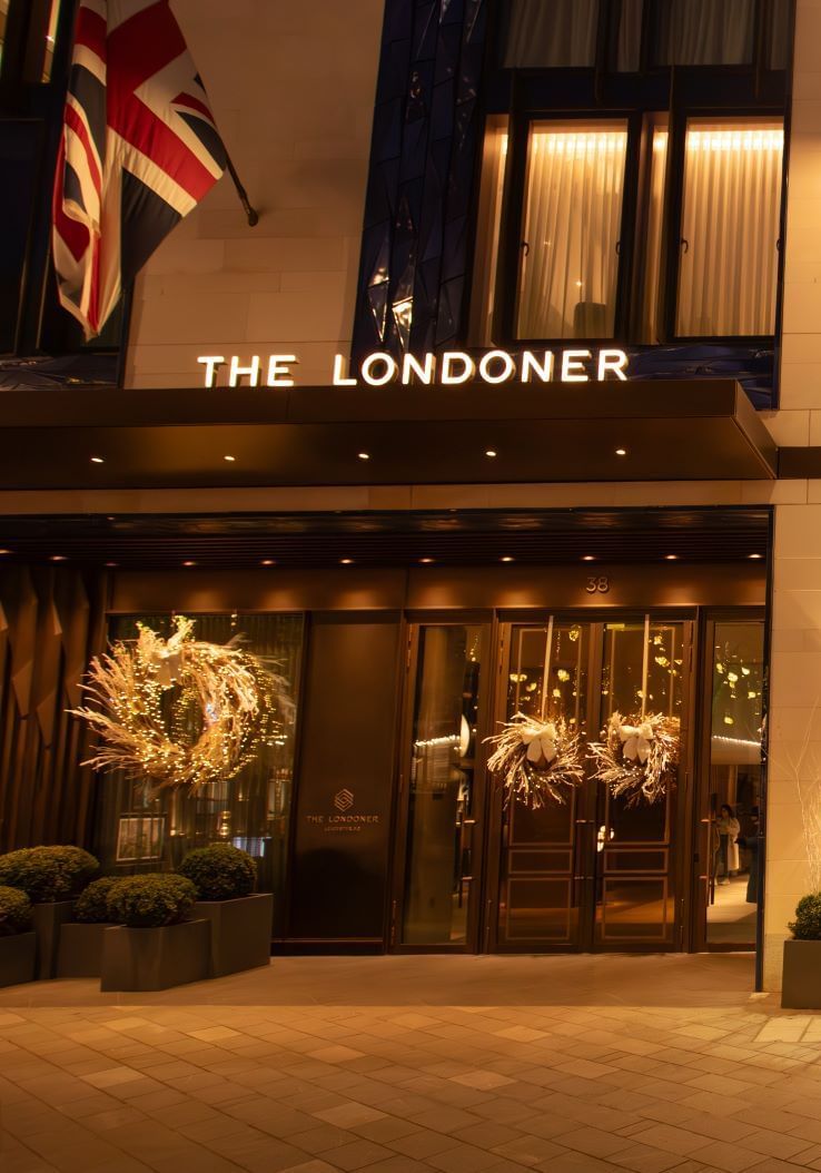The elegant exterior of The Londoner Hotel at night, adorned with festive wreaths and glowing lights