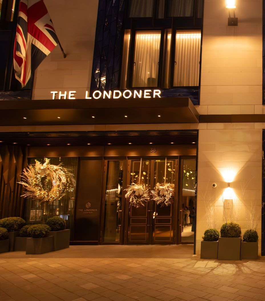 The elegant exterior of The Londoner Hotel at night, adorned with festive wreaths and glowing lights