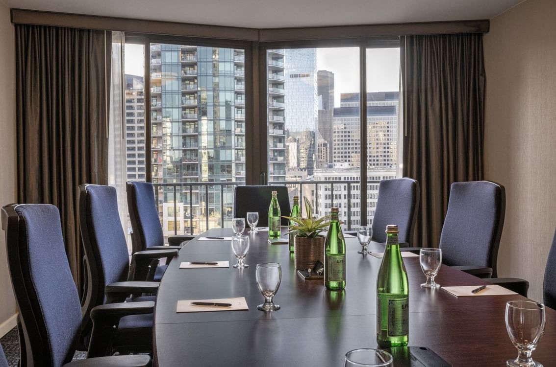 Meeting table featuring glass cups by water bottles under a large city window in Boardroom (1808) at Warwick Seattle