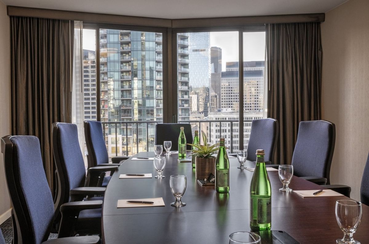 Meeting table featuring glass cups by water bottles under a large city window in Boardroom (1808) at Warwick Seattle