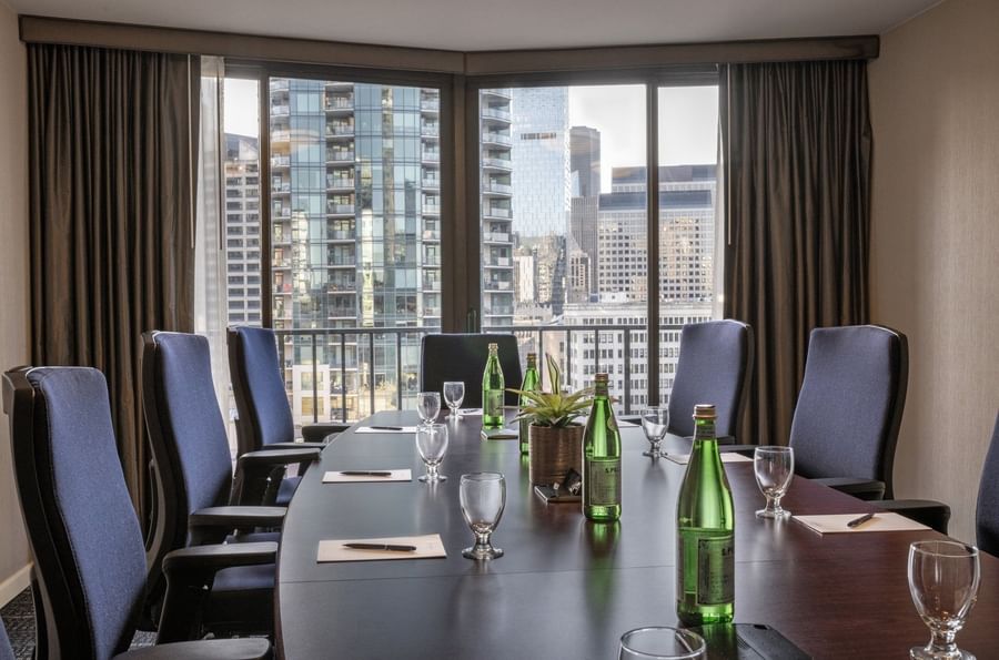 Meeting table featuring glass cups by water bottles under a large city window in Boardroom (1808) at Warwick Seattle