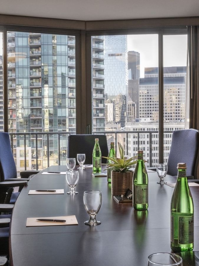 Meeting table featuring glass cups with water bottles under a large city window in Boardroom 1808 at Warwick Seattle