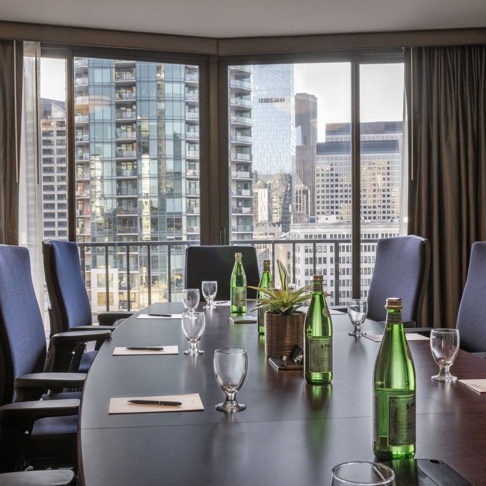 Meeting table featuring glass cups with water bottles under a large city window in Boardroom (1808) at Warwick Seattle