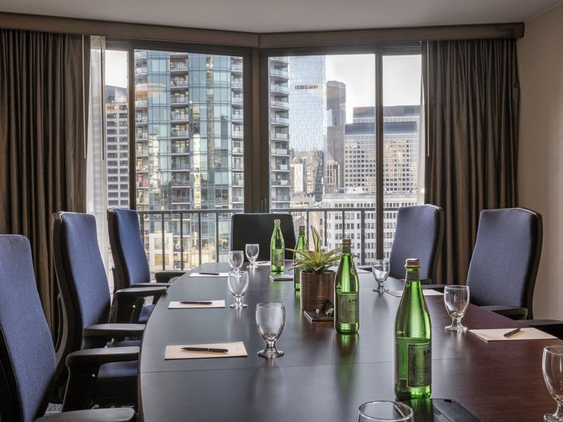 Meeting table featuring glass cups with water bottles under a large city window in Boardroom (1808) at Warwick Seattle